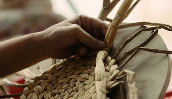 Kézműves nő kézzel fon egy IKEA SOARÉ kerek tányéralátétet.