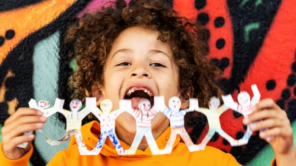 Kid smilling holding up a banner of cut out paper in people shaped design