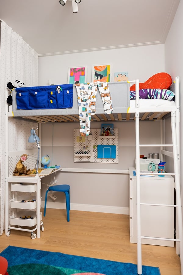 Kids’ bedroom with loft bed, study desk, blue stool, and colorful wall art.