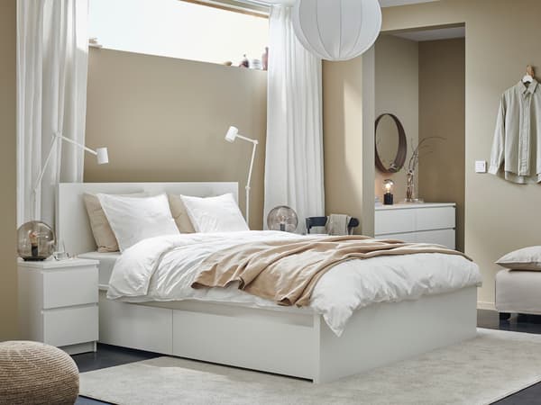 収納付き白いベッドに白い寝具を合わせた機能的な寝室。ベージュの壁と自然光で明るい雰囲気。