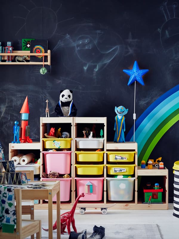 Kinderkamer met een krijtbordmuur waarop tekeningen zijn gemaakt en een regenboog- en sterrenlamp als decoratie.