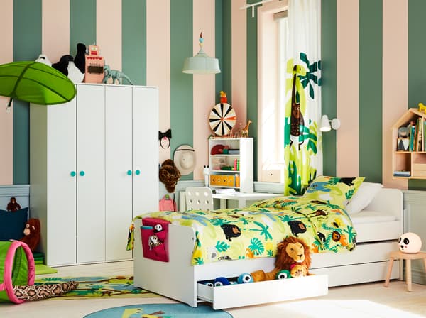 Kinderkamer met junglethema en een wit bedframe, knuffels, groen textiel met dierenprints en een baldakijn met bladmotief.