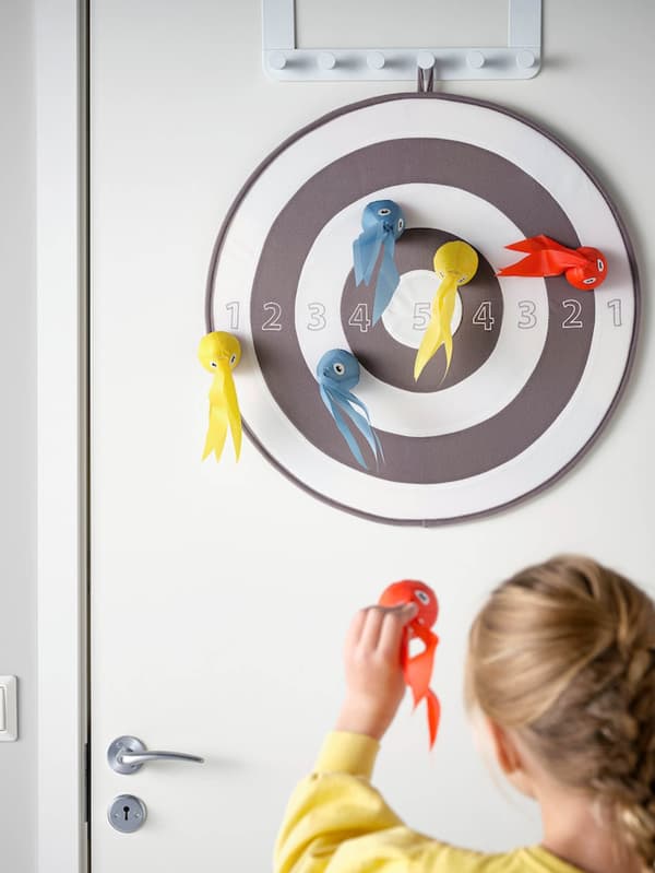 Kislány LUSTIGT dartsjátékkal dobál célba az ajtóra akasztott céltáblára.