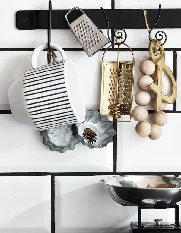 Kitchen accessories hanging on a black rail on white tiles.