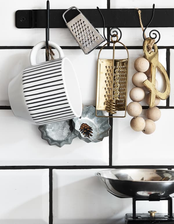 Kitchen accessories hanging on a black rail on white tiles.