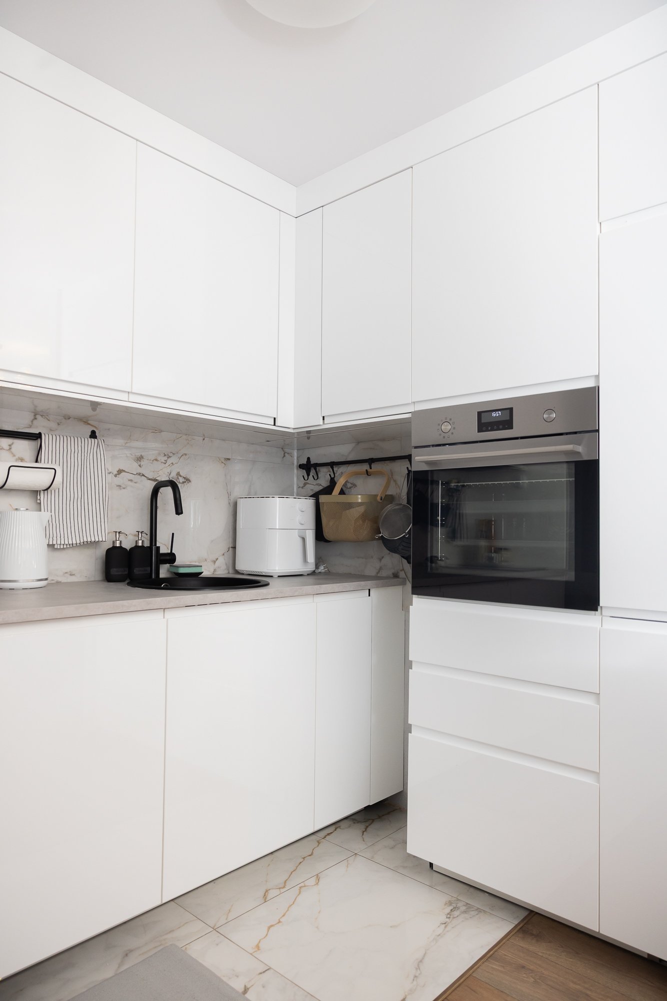 Kitchen corner with tall cabinets and a built-in oven, light cabinet fronts and a marble-effect worktop.