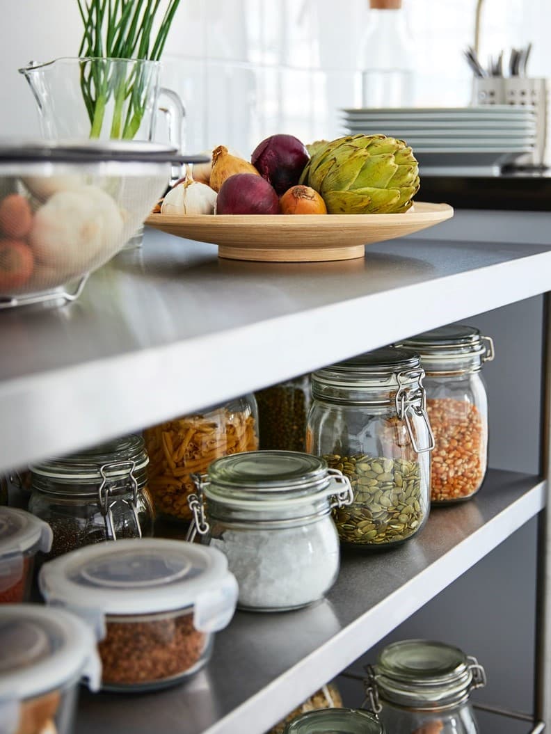 Kitchen countertop with glass jars filled with grains, cereals, and snacks, next to fresh fruits. 