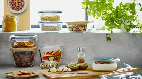 Kitchen countertop with multiple IKEA 365+ glass and plastic food containers with various assortment of food stored inside. 