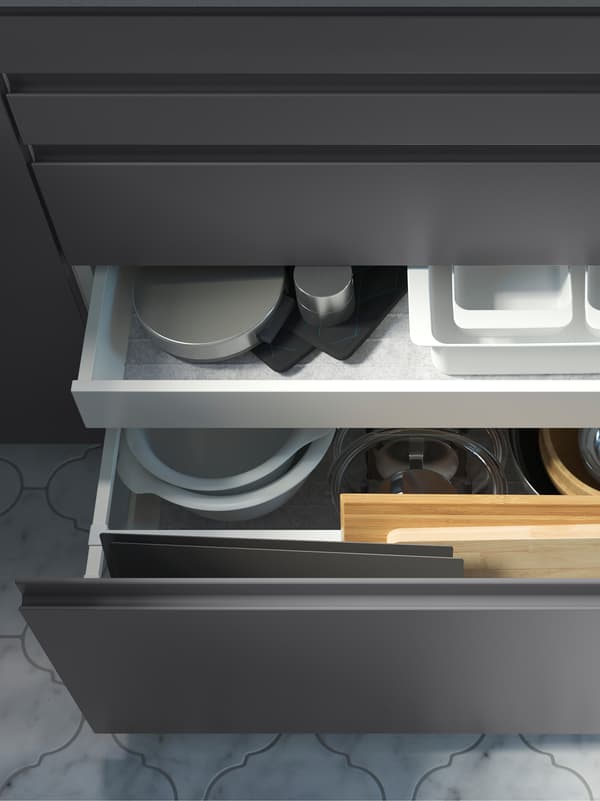 Kitchen cupboards with dark grey drawer fronts. One drawer is open and has another inside, and in both there are kitchen utensils stored.