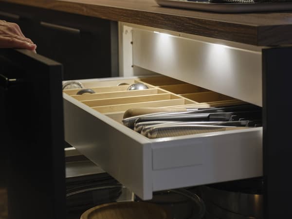 Kitchen drawer with bamboo organizer storing utensils and cutlery beneath a countertop.