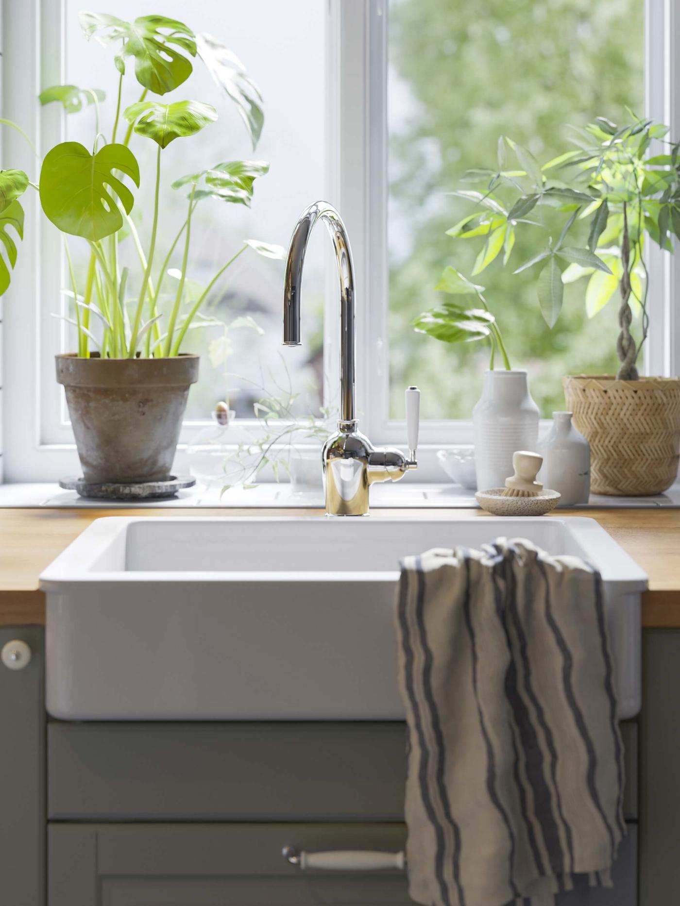 Kitchen sink with chrome faucet, striped towel, and potted plants by a bright window.
