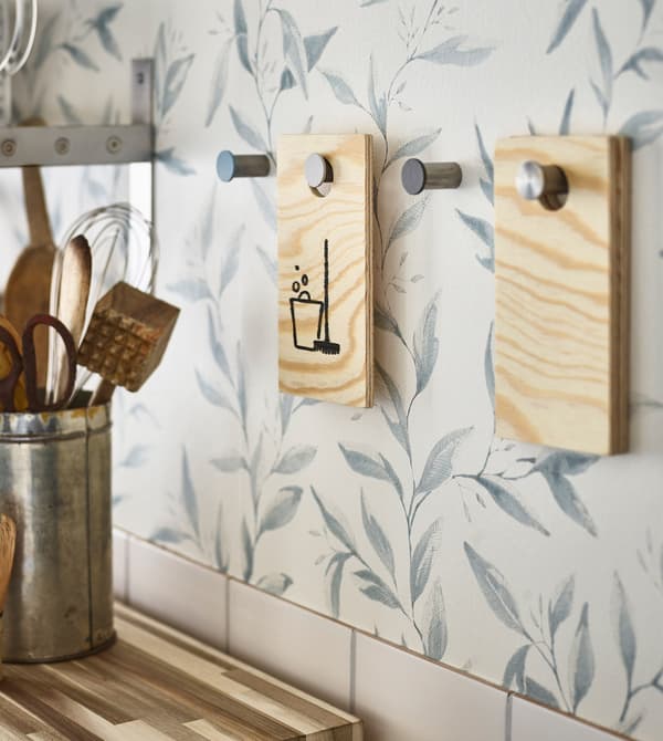 Kitchen utensils kept in a metal container and knobs on the wall holding DIY wooden chore tags.