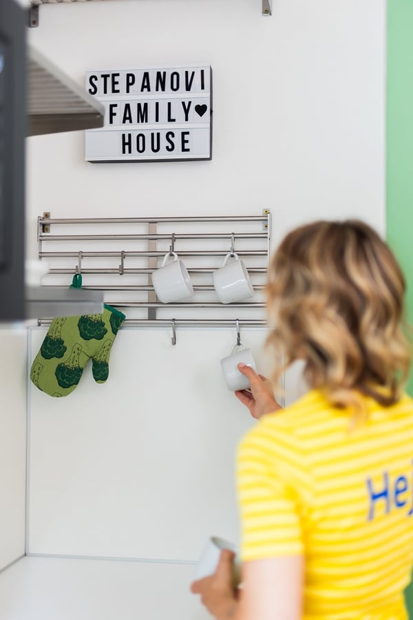 Kitchen wall detail with hanging mugs, oven mitts, and family house sign