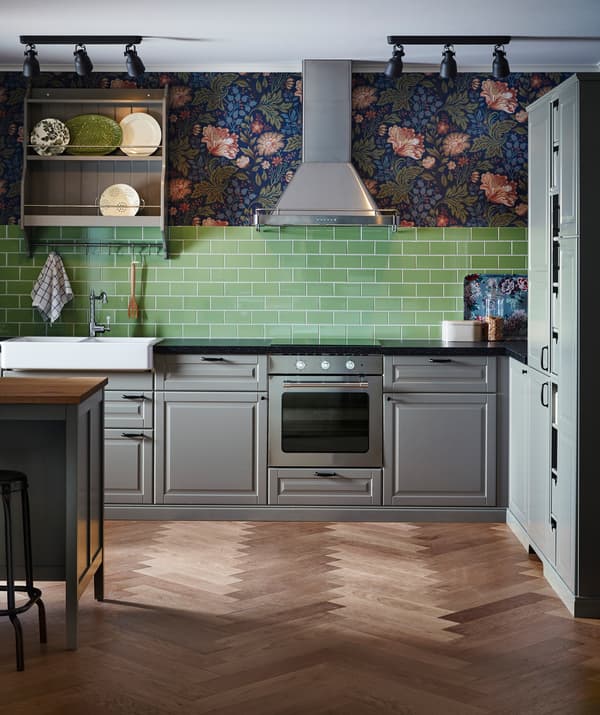 Kitchen with grey cupboards, green tiles, floral-patterned wallpaper and a stainless steel extractor hood.