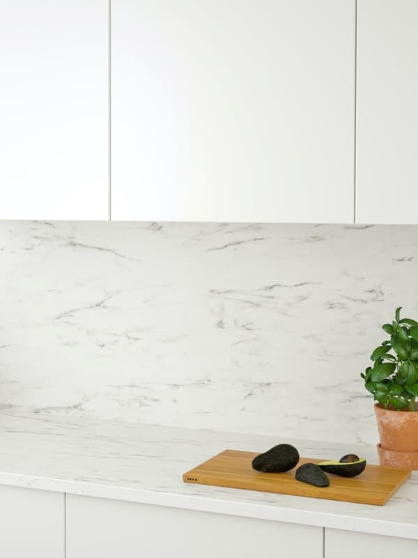 Kitchen with white fronts matching wall units and marble-like wall, on the worktop a cutting board and a potted plant