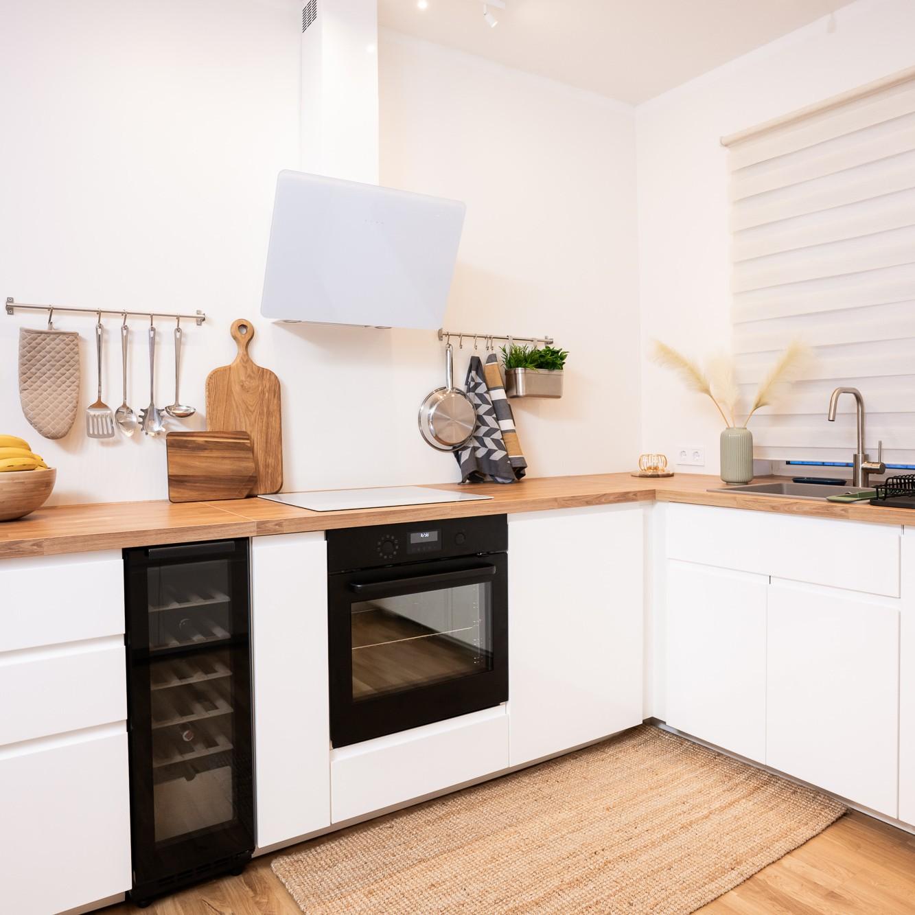 Kitchen work area with a built-in oven and hob, white cabinetry and wooden worktops; a wall panel and open shelves with crockery above the counter.