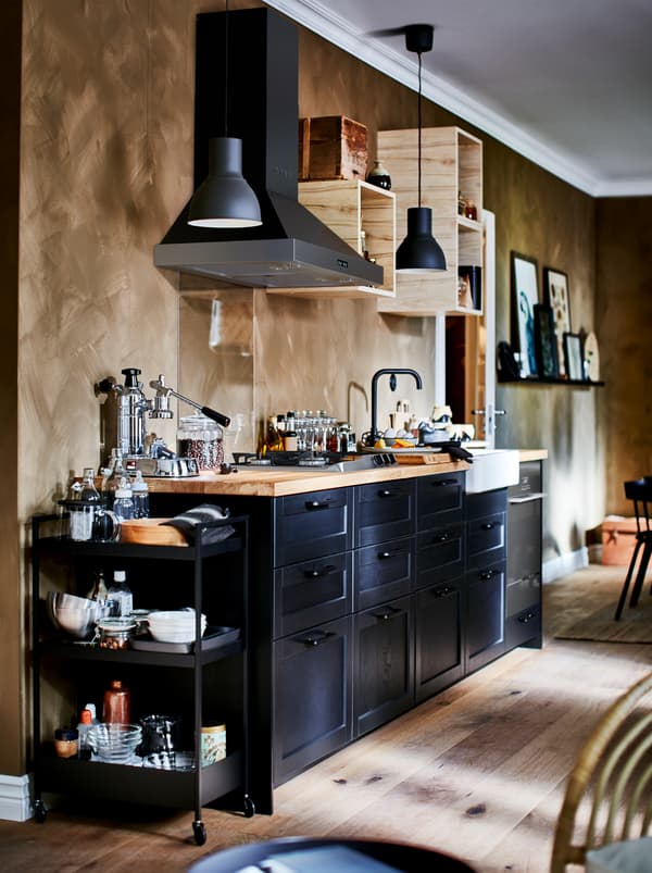 Kitchenette bien équipée avec petits éléments muraux ouverts, hotte et faces de tiroir LERHYTTAN foncées.