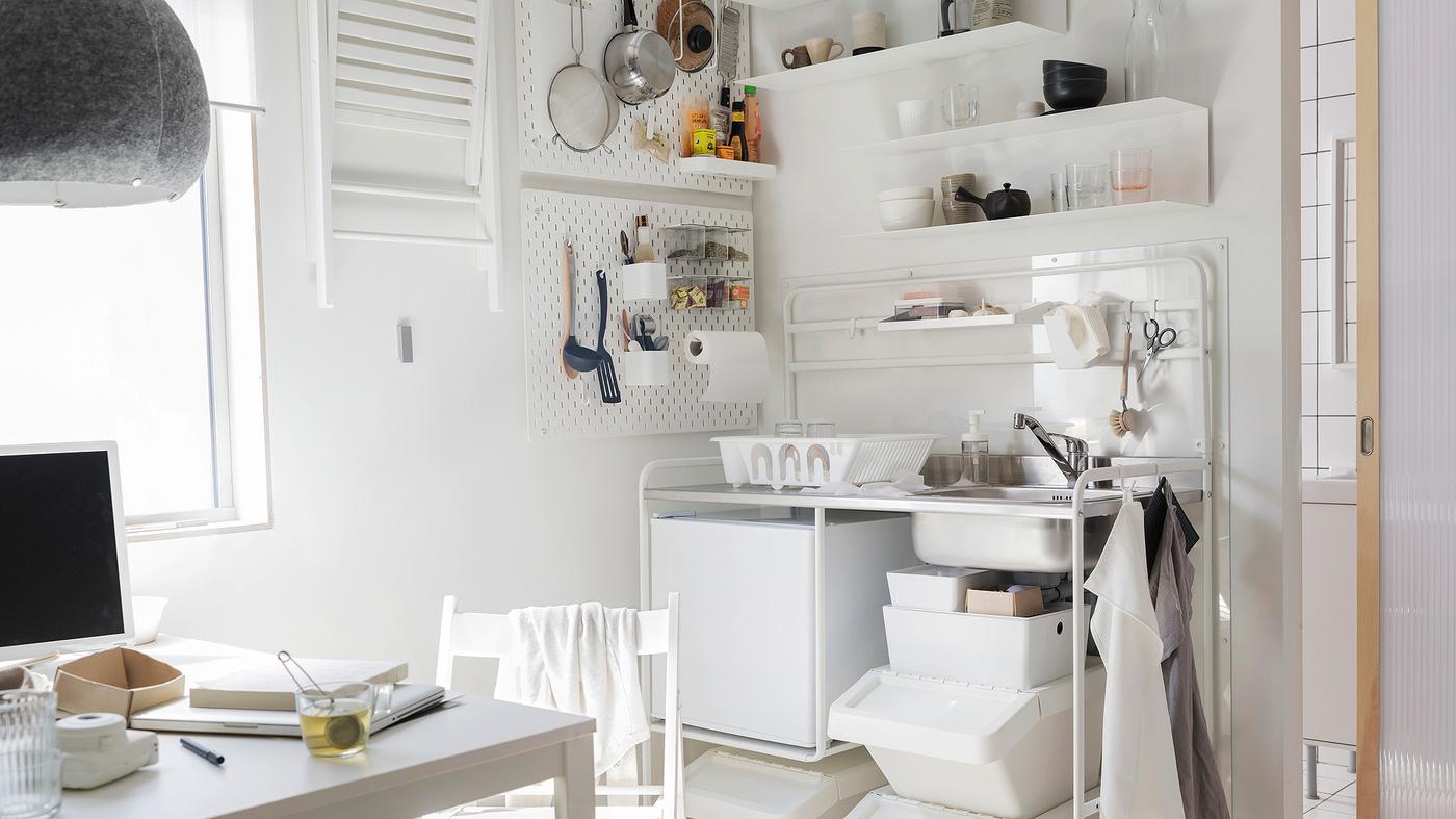 Kitchenette em branco com uma cozinha independente SUNNERSTA em branco, um frigorífico pequeno em branco e uma mesa e uma cadeira em branco.