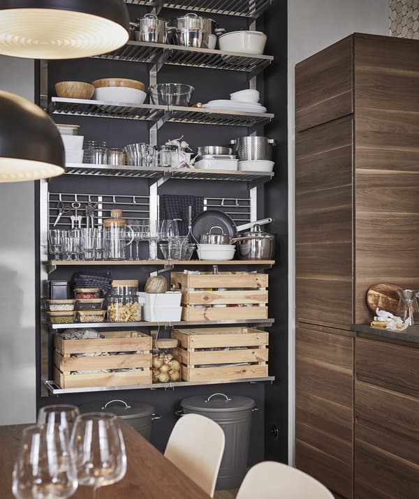 Kitchenware, tableware and wooden crates stored on a metal open storage unit against a dark wall.