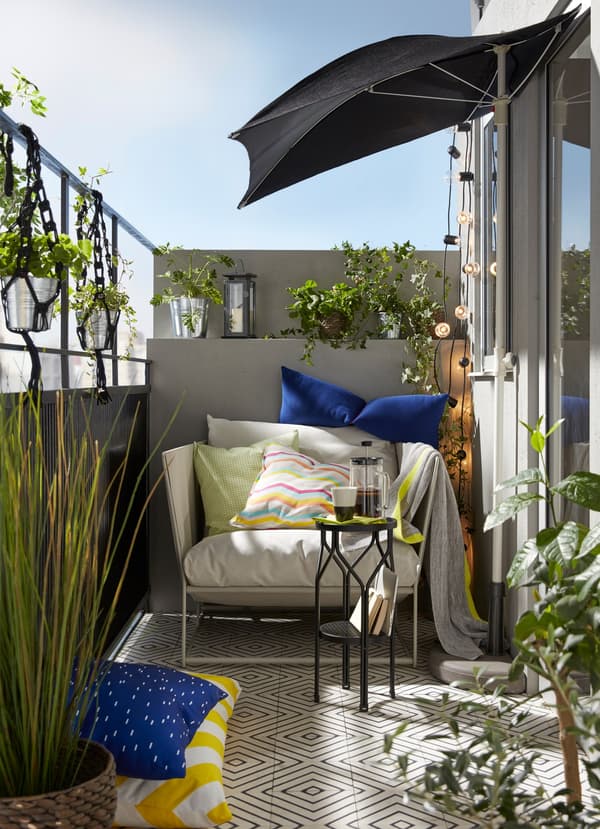 Klein balkon van een flat met planten, een blauwe parasol en een comfortabele beige HAVSTEN fauteuil voor binnen en buiten