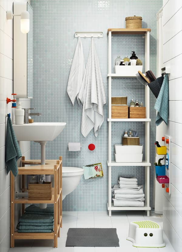 Kleine gezinsbadkamer met witte en lichtblauwe tegels en een grote witte DYNAN open kast gevuld met witte badkameraccessoires.