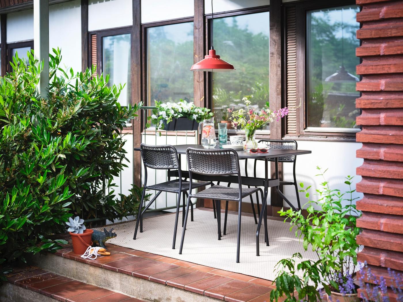 Kleiner Terrassen-Essbereich mit schwarzem Tisch und vier schwarzen Stühlen, umgeben von Pflanzen.