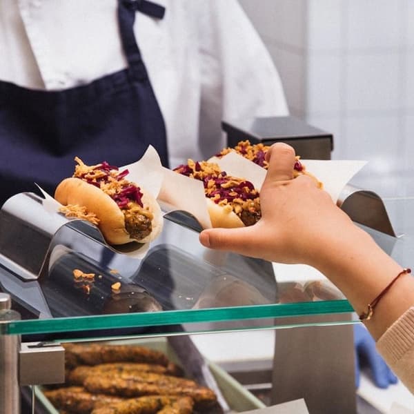 Klientam pār leti pasniedz svaigi pagatavotu hotdogu ar dārzeņu desiņu un piedevām.