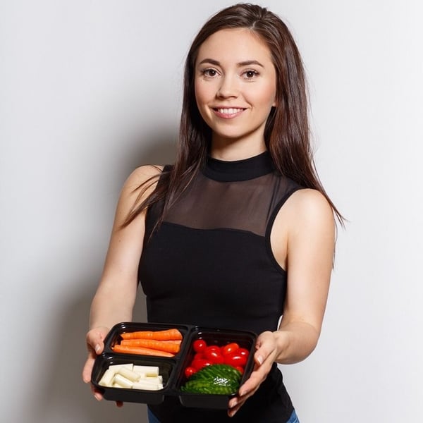 Klinta Stasjule - certified nutritionist and meal planning expert, dressed in black and holding dark plate with carrots, cherry tomatioes, cheese and cucumber