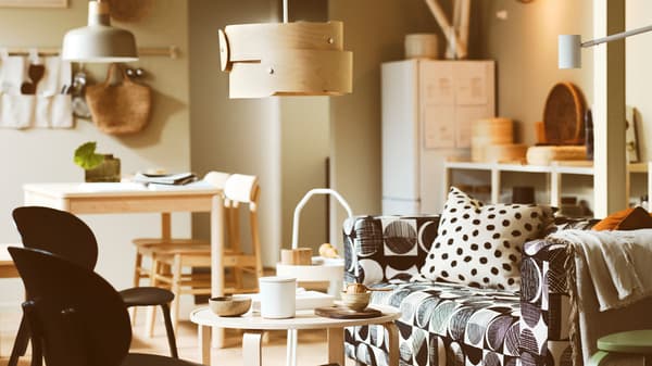 KLIPPAN zitbank met motief in zwart/beige, berken SÖDÅKRA hanglamp boven een berken salontafel en twee zwarte fauteuils.