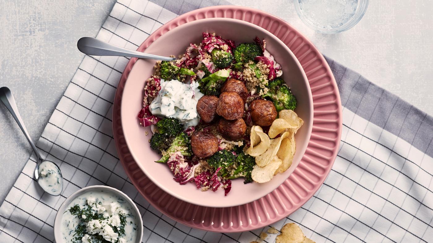 Klopsiki warzywne i sałatka z quinoa w różowej misce na różowym talerzu stojącym na biało-szarym, kraciastym ręczniku kuchennym.