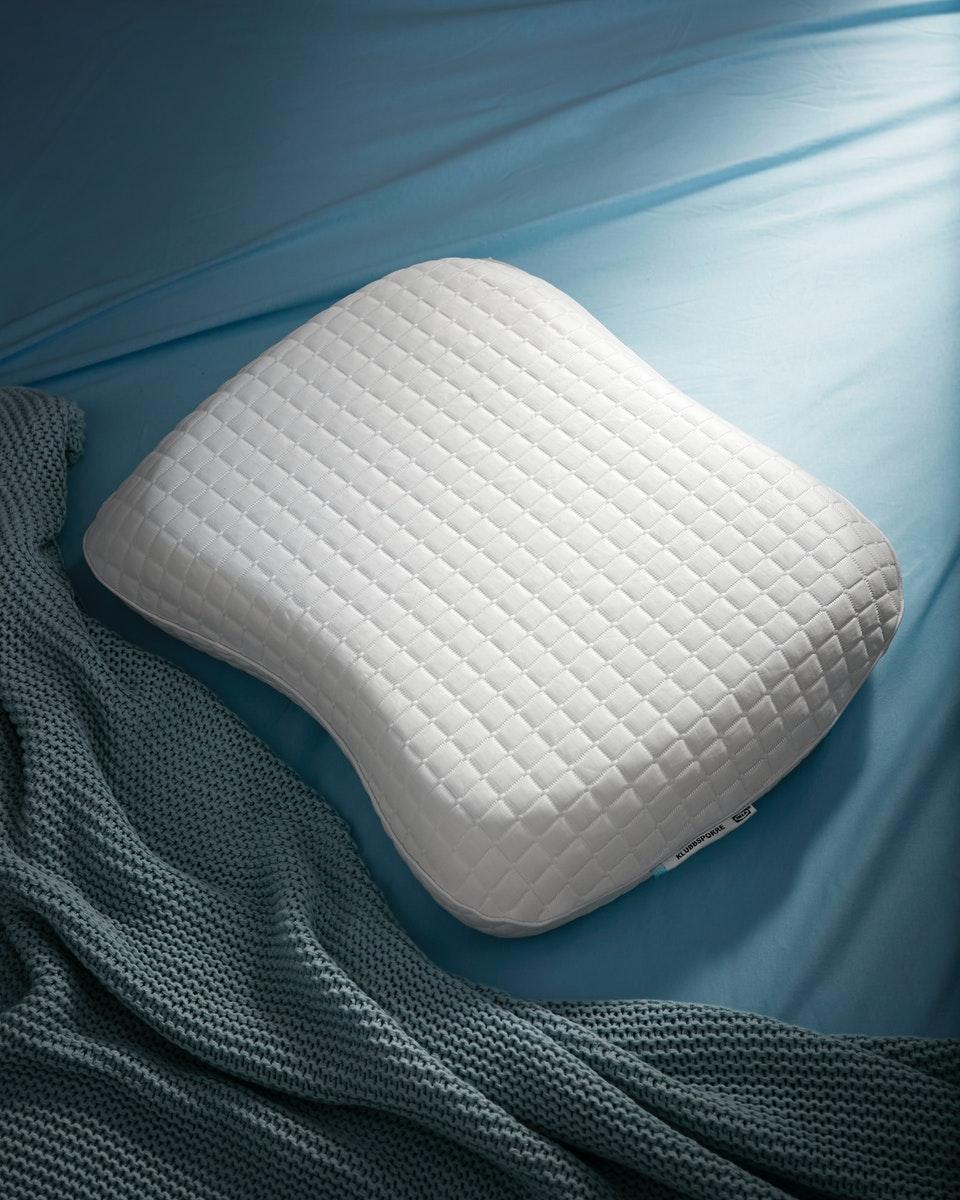 KLUBBSPORRE ergonomic pillow shown on a bed.