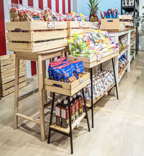 KNAGGLIG boxes filled with products and VANILJSTÅNG plant stands are displayed on wooden stools.