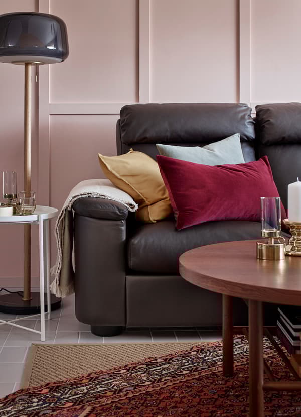 كنبة جلد بني داكن مزينة بوسائد SANELA أحمر، وأزرق فاتح وأصفر، مع سجادة حياكة مسطحة HELLESTED لون طبيعي وبني وبيج من أسفل.