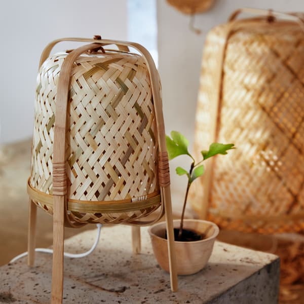 KNIXHULT table lamp is shown standing on four bent wood legs that encase its cylindrical shape woven from many bamboo shades.