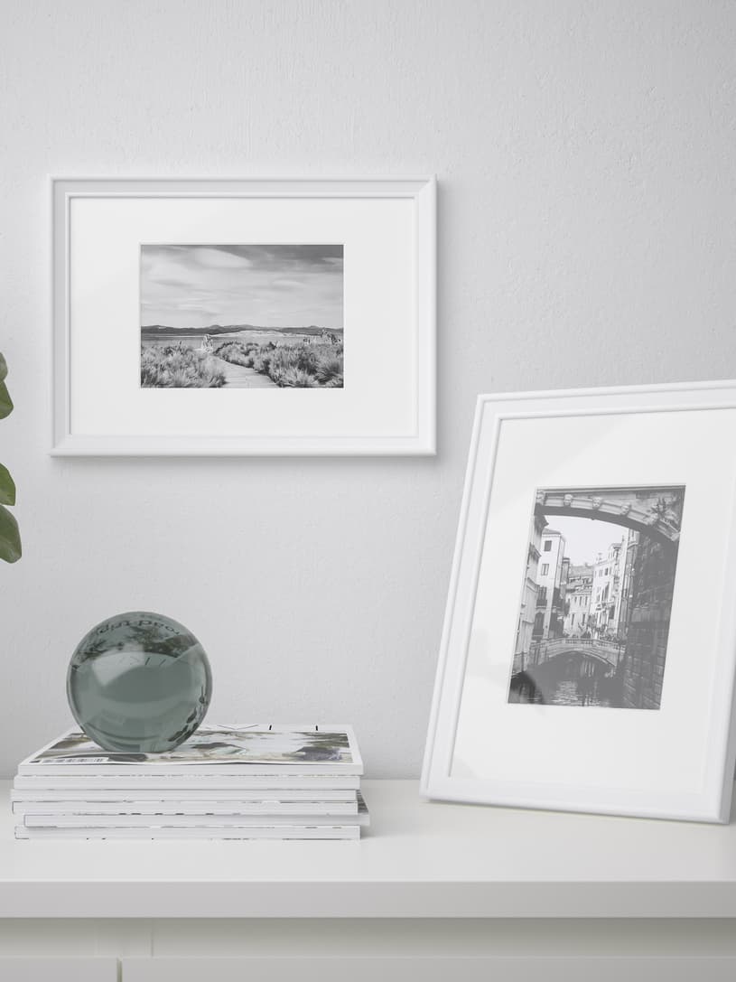 KNOPPÄNG photo frames standing on top of a storage cabinet and mounted on a white wall above a storage cabinet.
