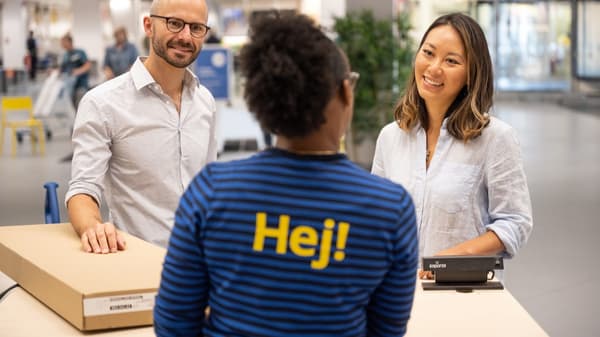 Kobieta i mężczyzna rozmawiają z osobą pracującą w IKEA przy ladzie, na której znajduje się paczka z produktem IKEA. 