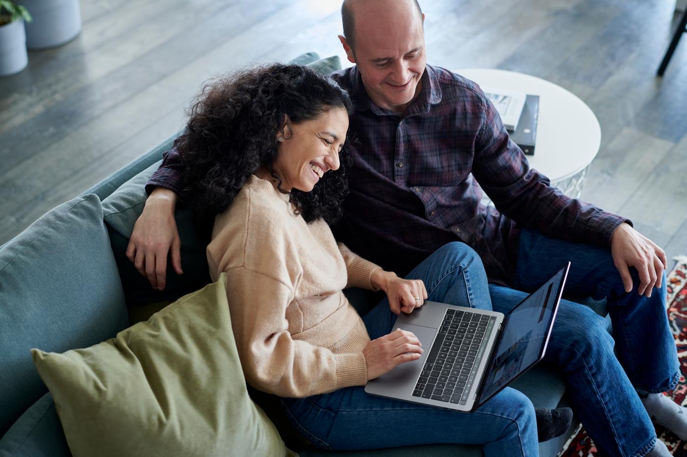 Kobieta i mężczyzna siedzą na kanapie z laptopem na kolanach.