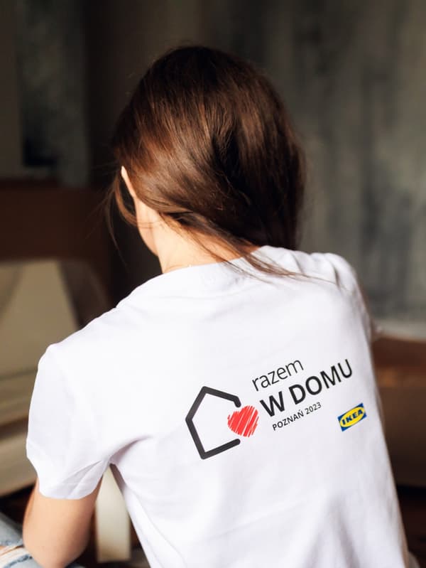 Kobieta odwrócona plecami w białej koszulce z napisem "Razem w domu". 