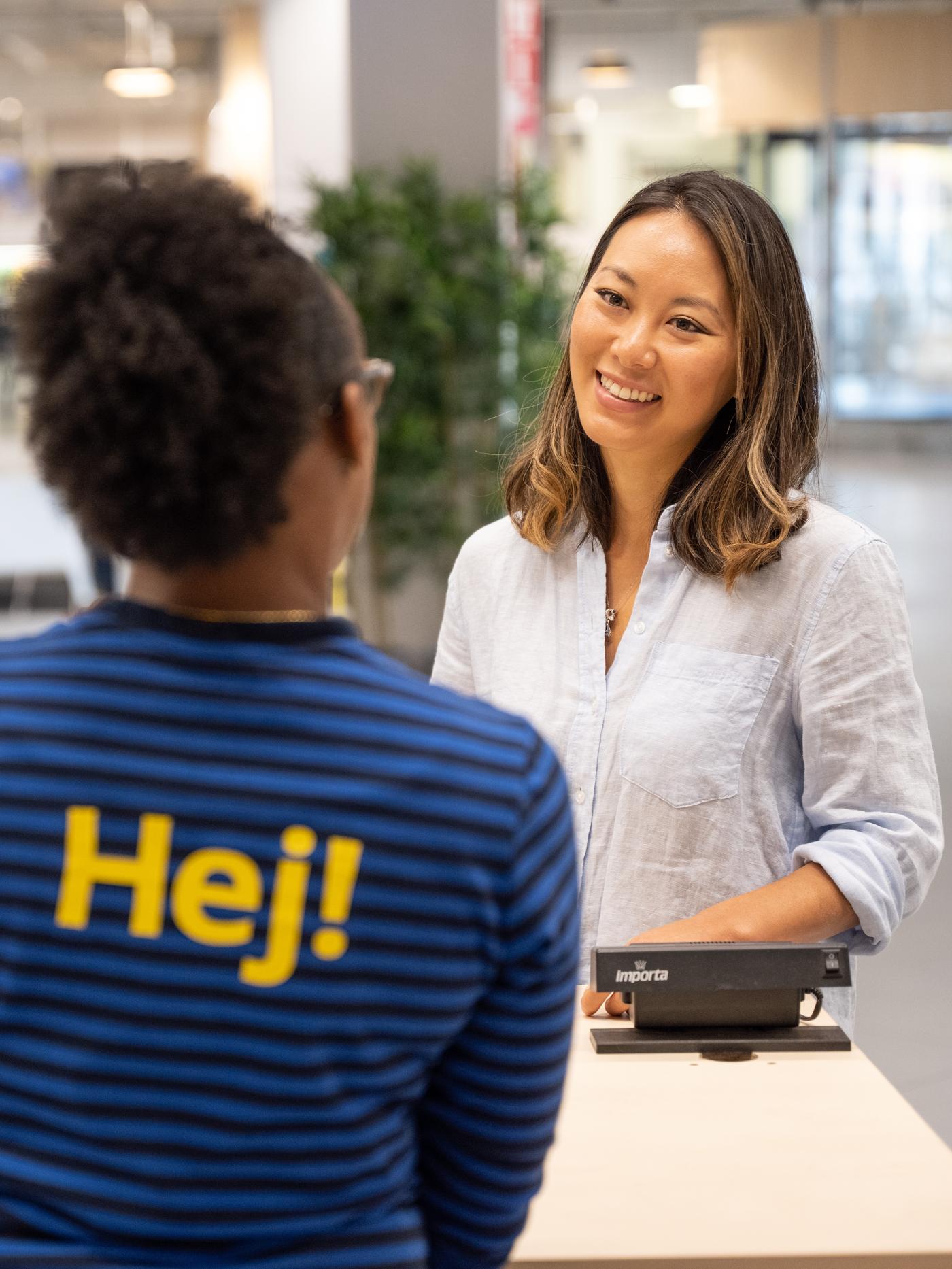 Kobieta w niebieskiej bluzce w paski rozmawia z kobietą w białej koszulki w Dziale Obsługi Klienta.