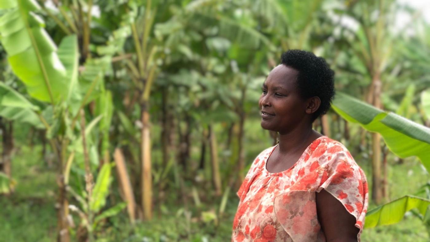 kobieta z Rwandy w sukience w czerwone kwiatki stoi na tle palm