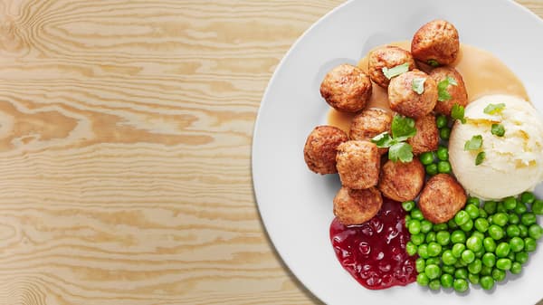 Köttbullar, potatismos, lingon och ärtor på en vit tallrik.