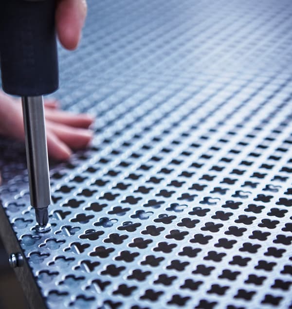 Közeli kép egy fémhálós panelről, amit valaki az IKEA polc hátsó részéhez csavaroz éppen.