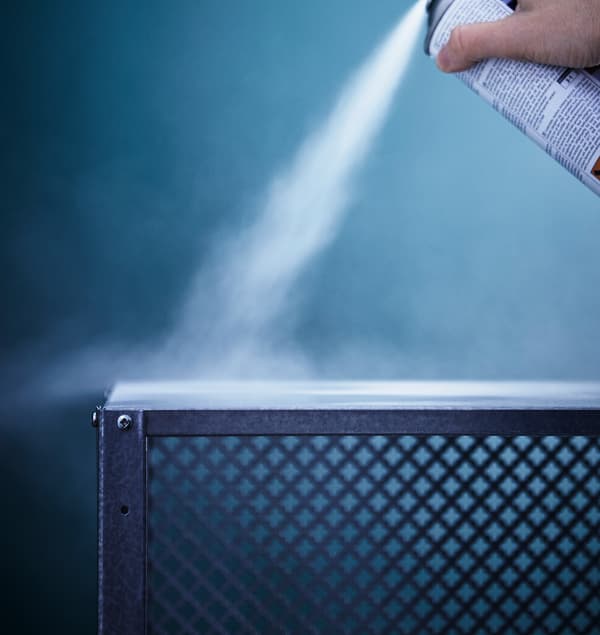 Közeli kép egy IKEA polcról, ait éppen fehér festékkel fújnak át.