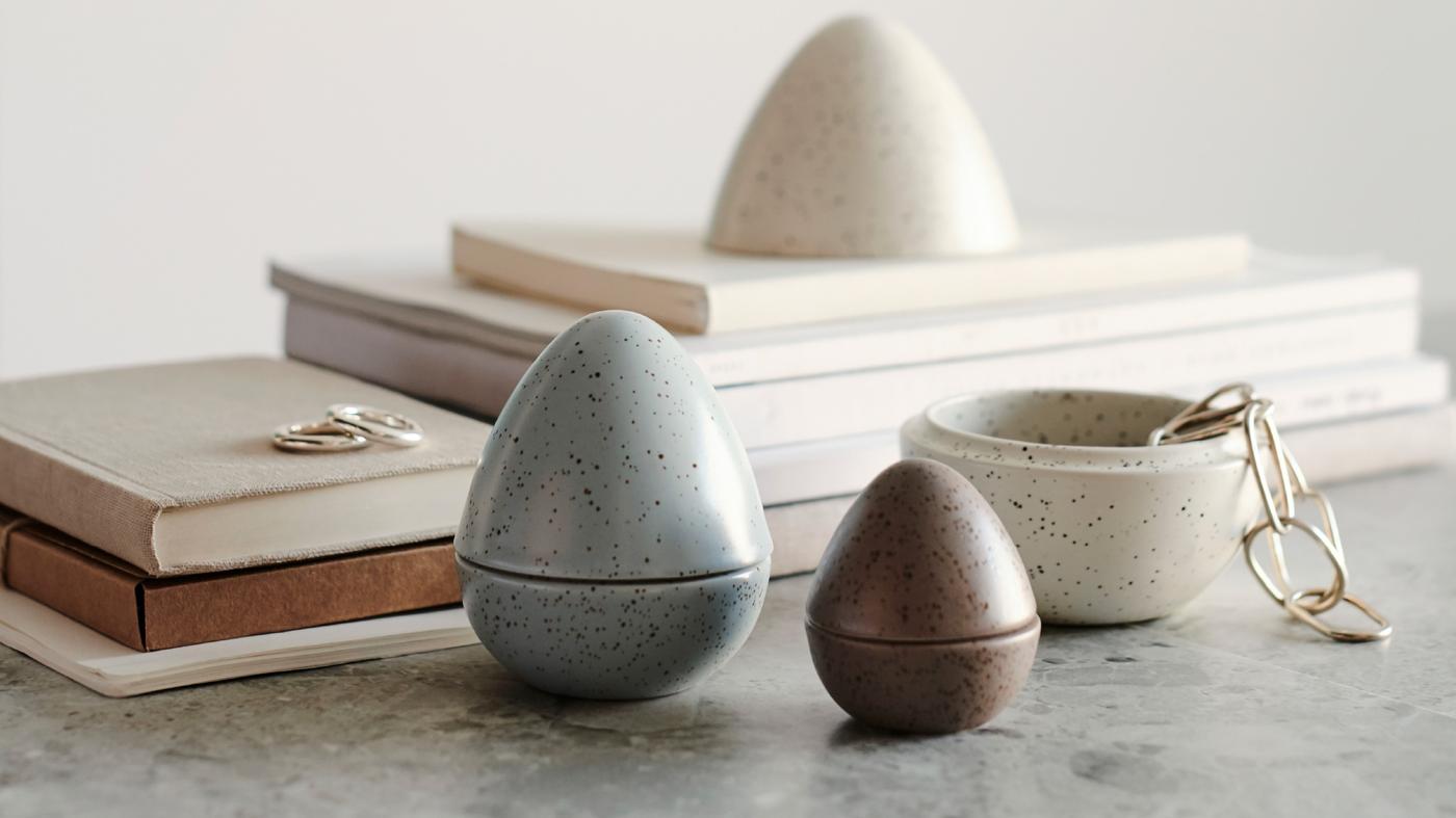 Közeli kép egy RÅDFRÅGA dísztojás-kollekcióról és könyvekről. Az egyik tojás ki van nyitva és egy ékszer látszik benne.