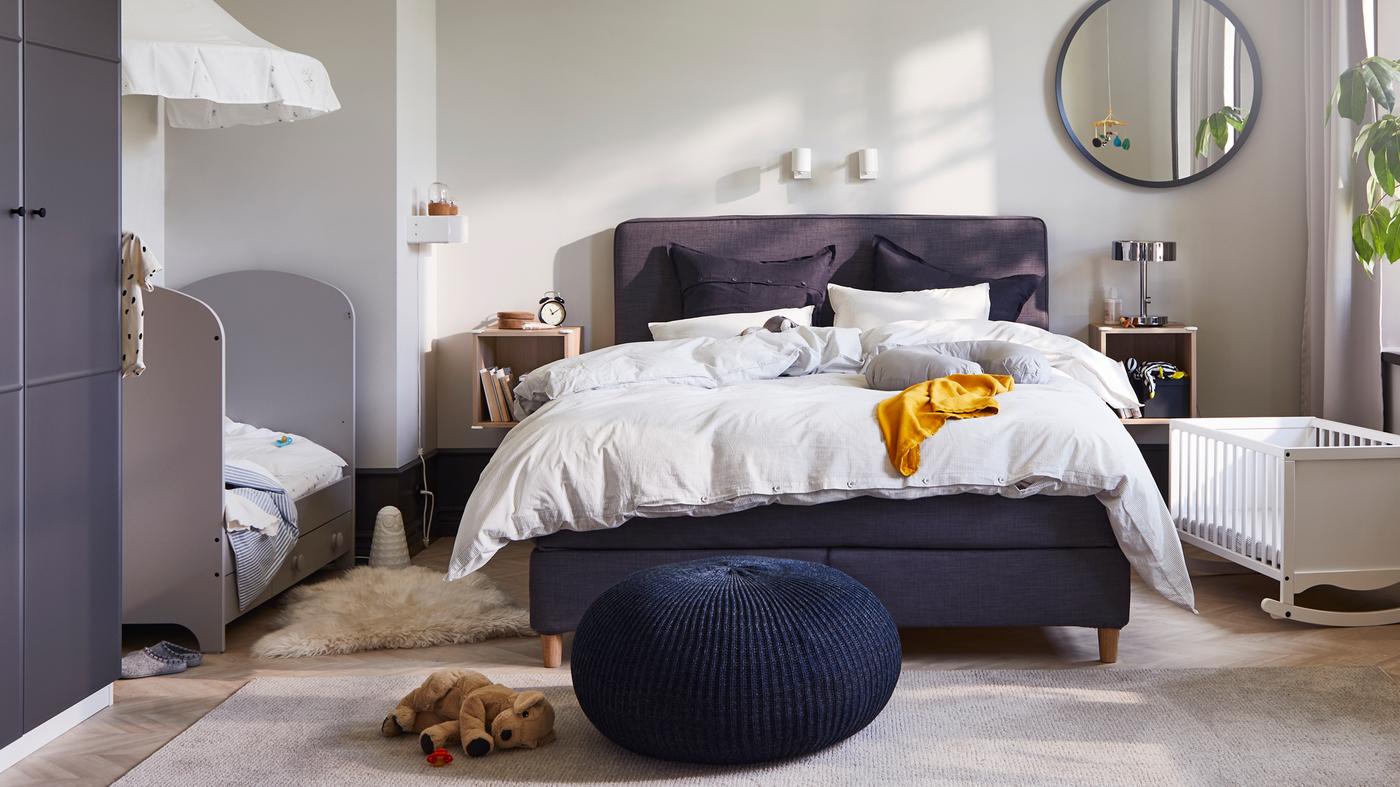 Közös hálószoba a szülőknek és két gyereknek, ahol egy DUNVIK dívány áll egy GONATT rácsos ágy és egy fehér SOLGUL bölcső között.