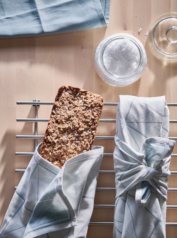 Køkkenbord med et glas med salt og to fuldkornsbrød pakket ind i SANDVIVA viskestykker på en LÄMPLIG bordskåner.