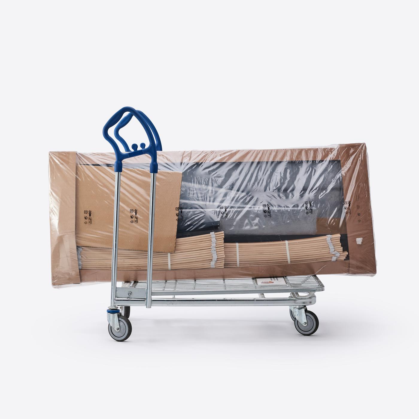 Kolica za teret s paketima omotanim folijom. Kolica su metalna, a paketi su kartonske kutije omotane prozirnom plastičnom folijom, spremne za transport ili dostavu.