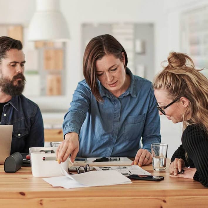 Kolme aikuista seisoo pöydän ympärillä suunnittelemassa.
