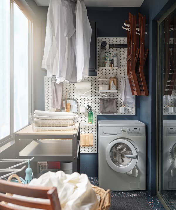 Kompakt mosóhelyiséggé alakított erkély, mosógéppel, fali kiegészítőkkel és száradó ruhákkal.