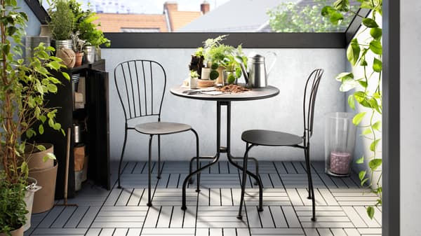 Kompakter Stadtbalkon mit schwarzem Bistro-Set, Pflanzregal und viel frischem Grün für ein urbanes Gartenfeeling.
